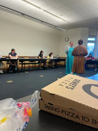 Box of pizza in the foreground with students performing in the background