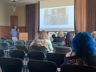 A slide show the movie Julius Caesar with Erdman talking and gesturing to a group of high school students 