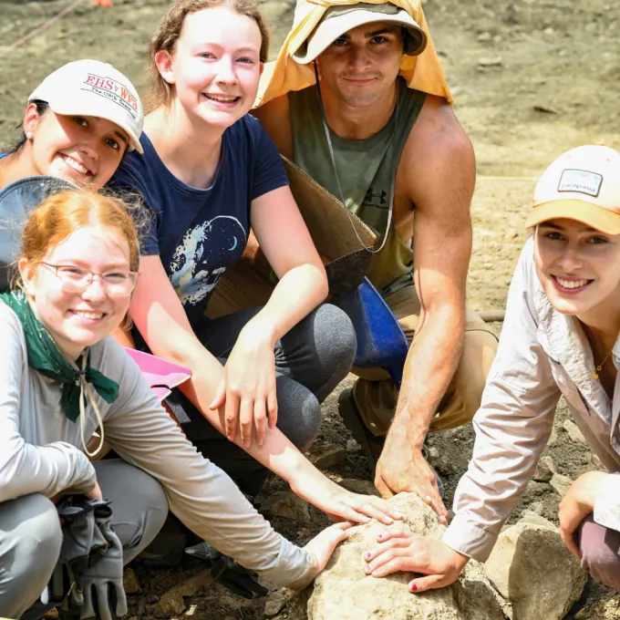 Held with group of students with their hands touching an archeological find