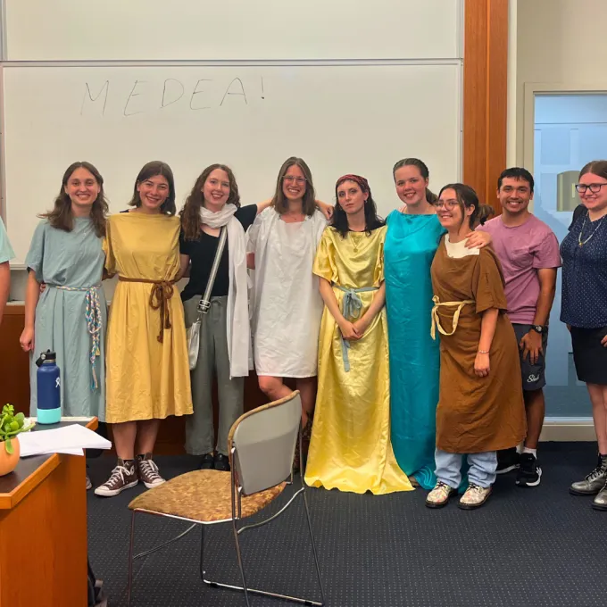 11 students lined up, some in costumes of greek tunics