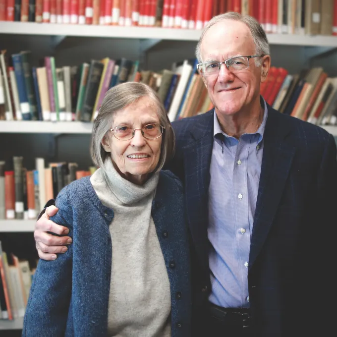 John with his arm around Penelope standing in front of a library of books